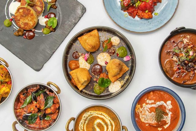 A vibrant flat lay of contemporary Indian dishes including samosas, chicken tikka, and rich curries, showcasing our midweek set lunch offering in Petts Wood.