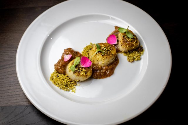 Perfectly seared king scallops presented on a vibrant chutney and garnished with a pistachio crumble, showcasing a contemporary Indian starter for our Father's Day menu in Petts Wood.