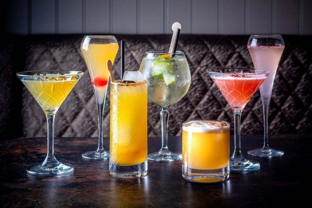 A row of handcrafted cocktails infused with Indian botanicals like curry leaves and lemongrass, designed to complement our contemporary Petts Wood dining experience.
