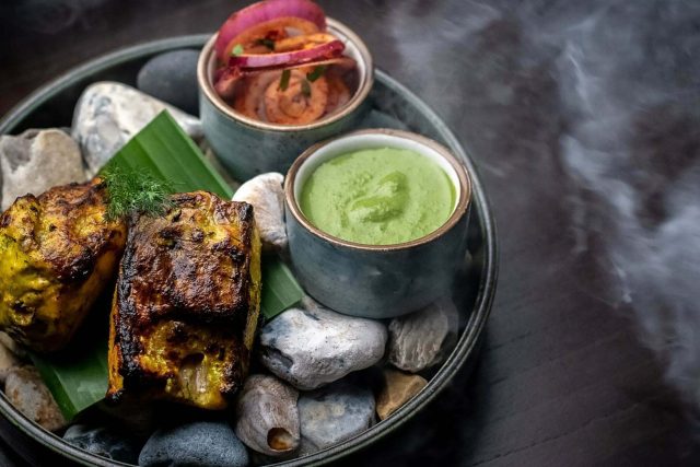 A rustic presentation of tandoori chicken tikka resting on a bed of spiced red onions, served alongside fresh mint chutney at our contemporary Indian restaurant in Petts Wood.