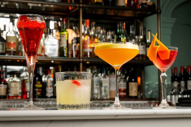 A vibrant selection of four signature cocktails and mocktails, including a tall red spritz and a classic martini, lined up on the marble bar at Indian Essence in Petts Wood.